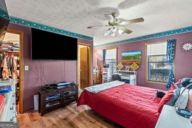 bedroom with a textured ceiling, wood finished floors, a ceiling fan, a spacious closet, and a closet