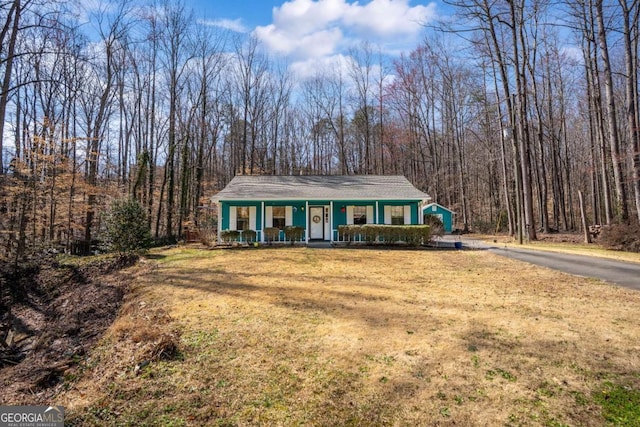 view of front of property featuring a front yard, covered porch, and a forest view