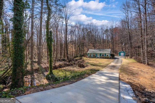 view of front of house featuring an outbuilding, concrete driveway, and a wooded view