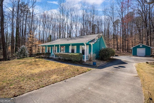 view of front of house featuring driveway, a detached garage, an outbuilding, covered porch, and a front lawn