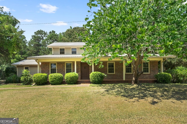 view of front of home featuring a front yard, covered porch, brick siding, and metal roof