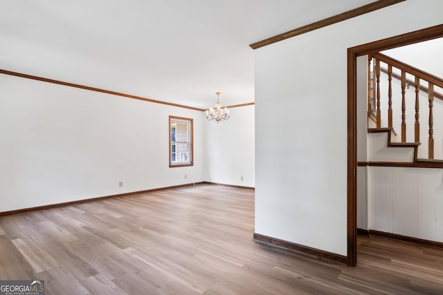 empty room featuring a notable chandelier, wood finished floors, baseboards, stairs, and crown molding