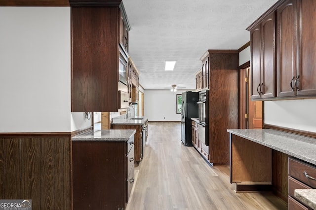 kitchen featuring light wood-type flooring, freestanding refrigerator, a sink, and dark brown cabinets