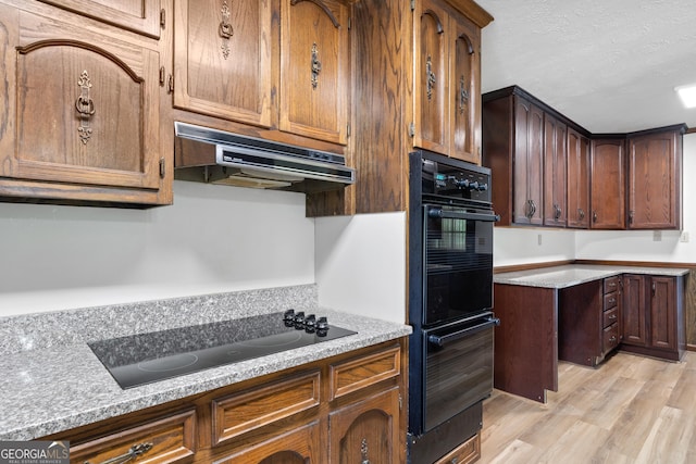 kitchen featuring light countertops, light wood-style floors, a textured ceiling, under cabinet range hood, and black appliances