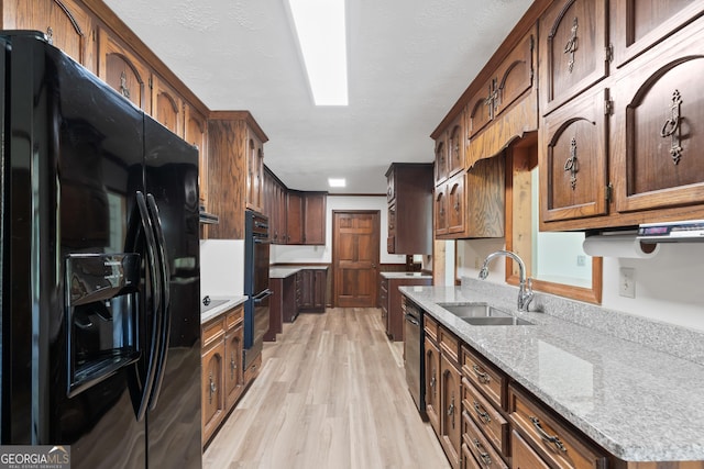 kitchen featuring light wood finished floors, light stone counters, a textured ceiling, black appliances, and a sink