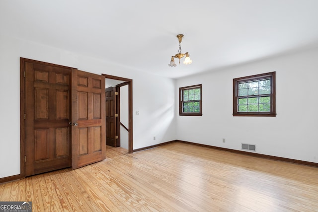 unfurnished room featuring a chandelier, light wood-style flooring, visible vents, and baseboards