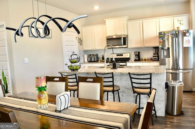 kitchen featuring dark wood-style floors, appliances with stainless steel finishes, light stone countertops, a kitchen island with sink, and a sink