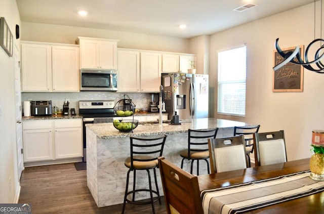 kitchen with visible vents, decorative backsplash, appliances with stainless steel finishes, white cabinetry, and an island with sink