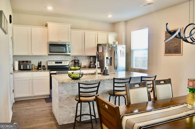 kitchen featuring stainless steel appliances, visible vents, white cabinets, backsplash, and a center island with sink