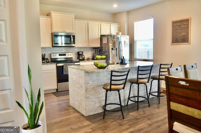 kitchen with tasteful backsplash, an island with sink, a breakfast bar area, light stone countertops, and stainless steel appliances