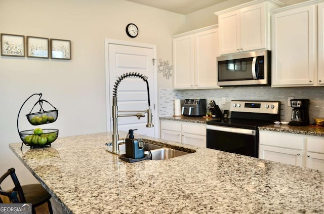 kitchen featuring appliances with stainless steel finishes, a sink, light stone counters, and tasteful backsplash