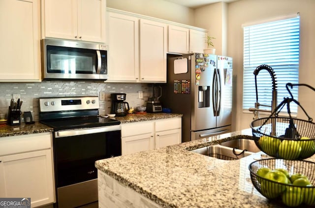 kitchen with appliances with stainless steel finishes, stone countertops, white cabinetry, and backsplash