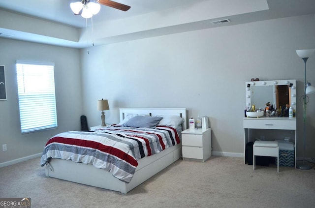 carpeted bedroom with a tray ceiling, a ceiling fan, visible vents, and baseboards