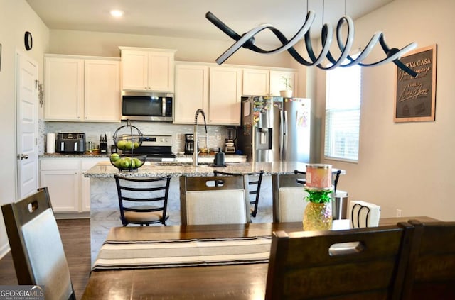 kitchen featuring a center island with sink, white cabinets, decorative backsplash, appliances with stainless steel finishes, and a sink