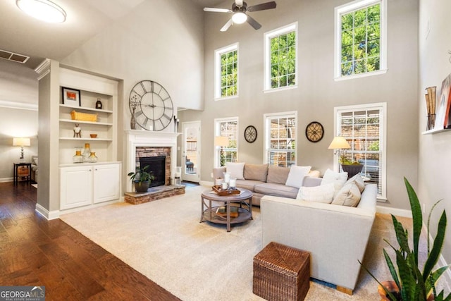 living area with ceiling fan, a stone fireplace, wood finished floors, visible vents, and baseboards