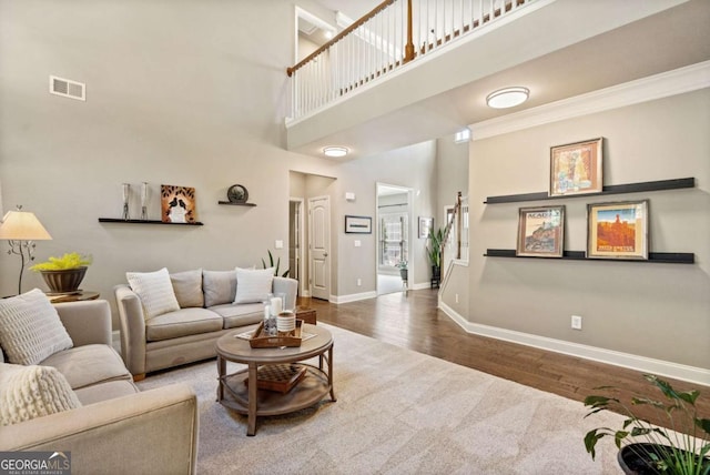 living area featuring a high ceiling, wood finished floors, visible vents, baseboards, and ornamental molding