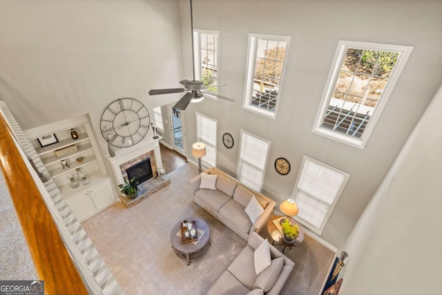 living area with a towering ceiling, ceiling fan, built in shelves, and a stone fireplace