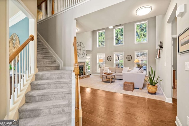 staircase featuring a stone fireplace, hardwood / wood-style floors, a towering ceiling, and baseboards