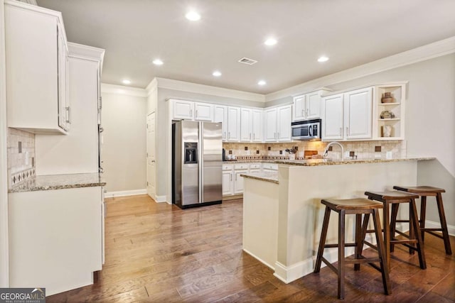 kitchen with stainless steel appliances, visible vents, white cabinets, light stone countertops, and a peninsula