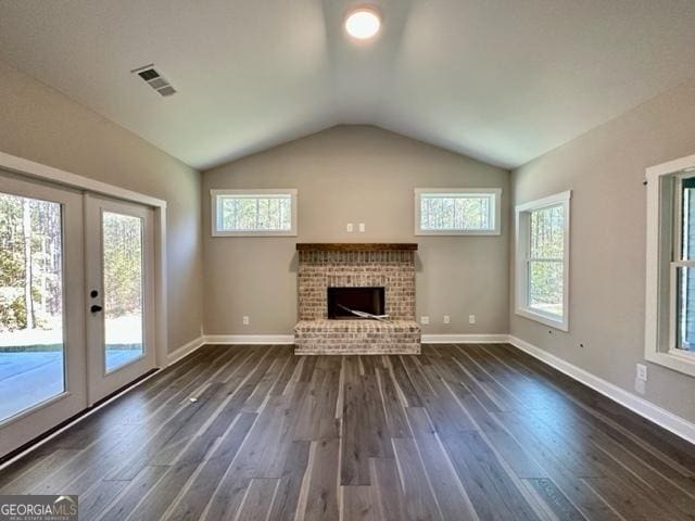 unfurnished living room featuring dark wood-style floors, visible vents, a brick fireplace, and a wealth of natural light