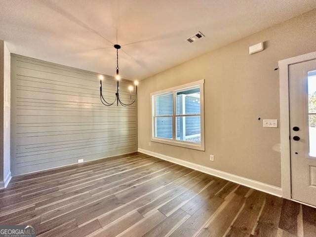 unfurnished dining area with an inviting chandelier, baseboards, visible vents, and dark wood finished floors