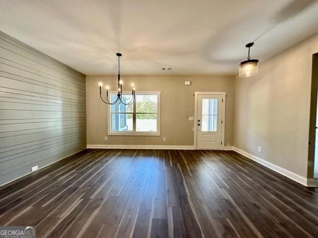 unfurnished dining area featuring a notable chandelier, dark wood finished floors, wood walls, and baseboards