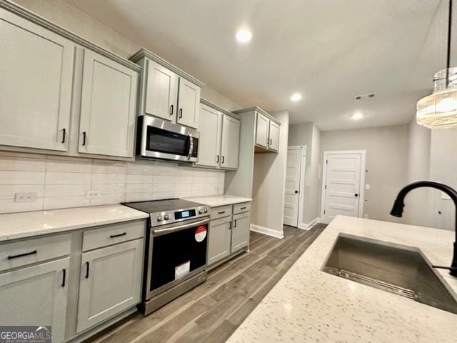 kitchen with dark wood-type flooring, a sink, appliances with stainless steel finishes, backsplash, and light stone countertops