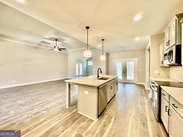 kitchen with french doors, appliances with stainless steel finishes, light wood-style floors, a sink, and an island with sink