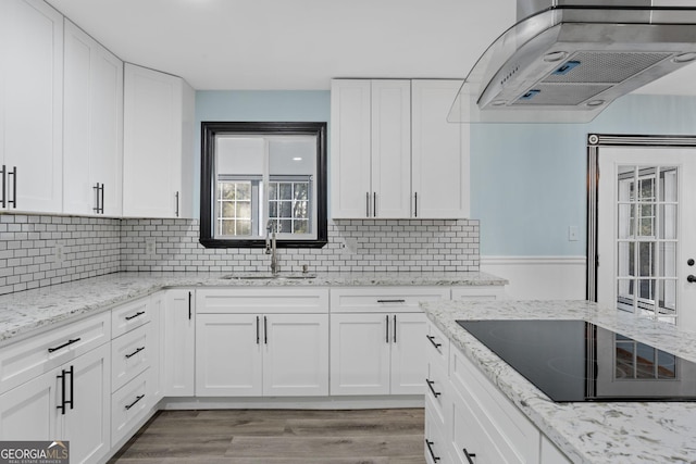 kitchen featuring light wood finished floors, range hood, black electric cooktop, white cabinetry, and a sink