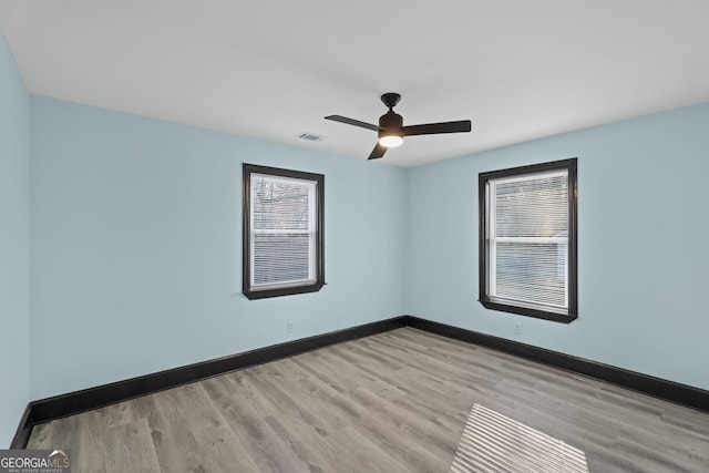 spare room featuring a ceiling fan, visible vents, baseboards, and wood finished floors