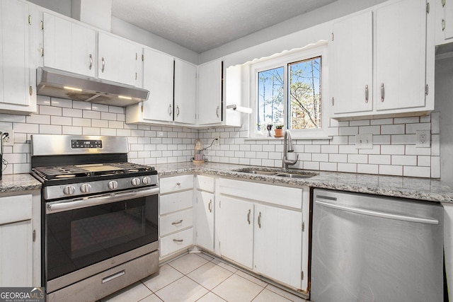 kitchen with light tile patterned floors, under cabinet range hood, a sink, white cabinetry, and appliances with stainless steel finishes