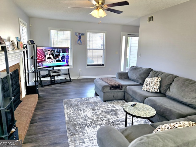 living room featuring dark wood-type flooring, visible vents, a fireplace, and a textured ceiling