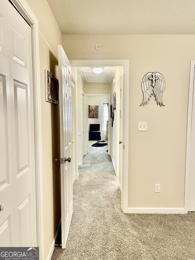 hallway with attic access, light colored carpet, and baseboards