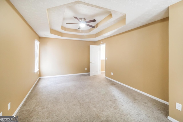 carpeted empty room featuring a raised ceiling, a ceiling fan, and baseboards