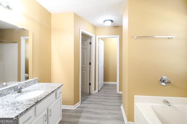 full bathroom featuring baseboards, toilet, a bathing tub, a textured ceiling, and vanity