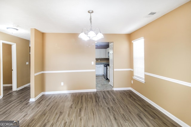 spare room featuring a notable chandelier, wood finished floors, visible vents, and baseboards