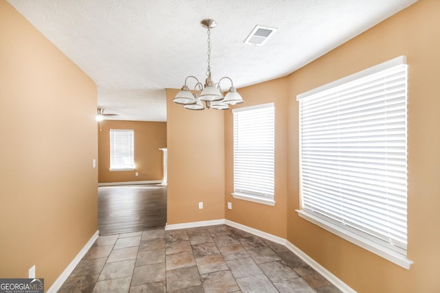 unfurnished dining area featuring visible vents, a textured ceiling, baseboards, and ceiling fan with notable chandelier