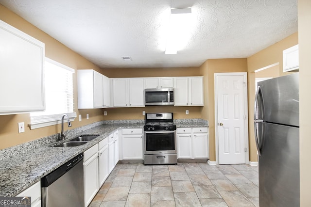 kitchen featuring light stone counters, stainless steel appliances, visible vents, white cabinets, and a sink