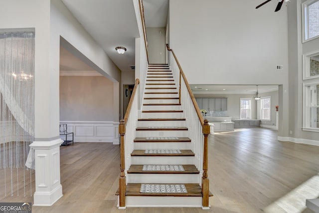 stairs featuring a decorative wall, wood finished floors, a ceiling fan, wainscoting, and decorative columns