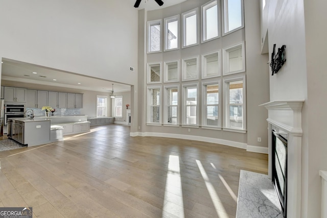 unfurnished living room featuring light wood finished floors, a fireplace, a high ceiling, and baseboards