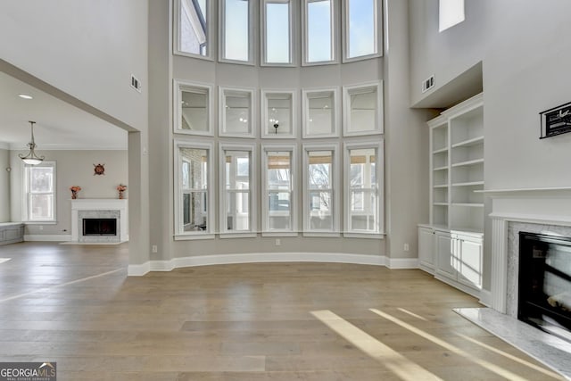 unfurnished living room featuring baseboards, visible vents, light wood finished floors, and a premium fireplace