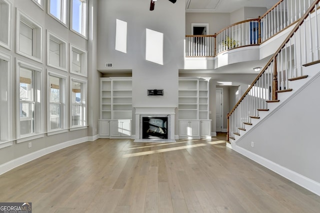 unfurnished living room featuring a high ceiling, a ceiling fan, a glass covered fireplace, wood finished floors, and baseboards