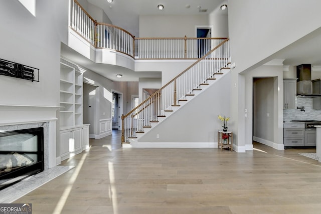 unfurnished living room with a fireplace, a towering ceiling, stairway, light wood-type flooring, and baseboards