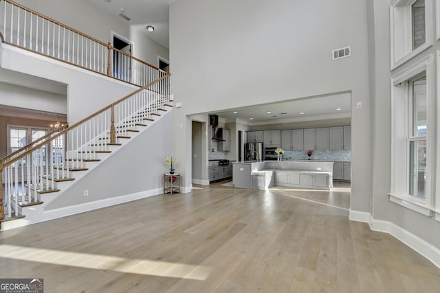 unfurnished living room featuring light wood-type flooring, visible vents, a high ceiling, and baseboards