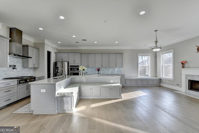 kitchen featuring appliances with stainless steel finishes, light countertops, gray cabinetry, light wood-type flooring, and wall chimney range hood