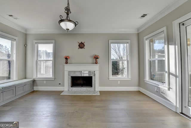 unfurnished living room with ornamental molding, a premium fireplace, visible vents, and light wood-style floors