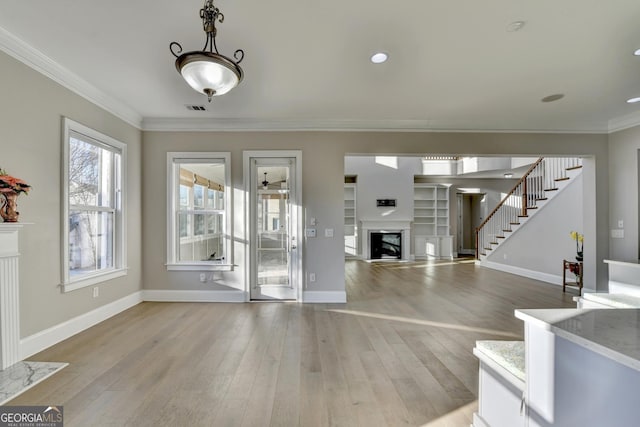 unfurnished living room with a fireplace, visible vents, ornamental molding, light wood-style floors, and stairs