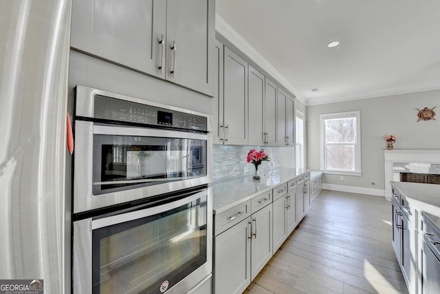 kitchen featuring backsplash, ornamental molding, appliances with stainless steel finishes, light wood-type flooring, and baseboards