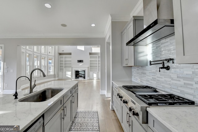 kitchen featuring stainless steel appliances, a sink, light wood-type flooring, wall chimney exhaust hood, and crown molding