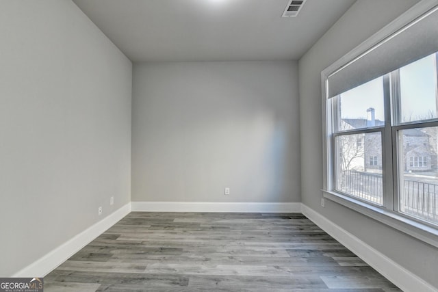 empty room with wood finished floors, visible vents, and baseboards